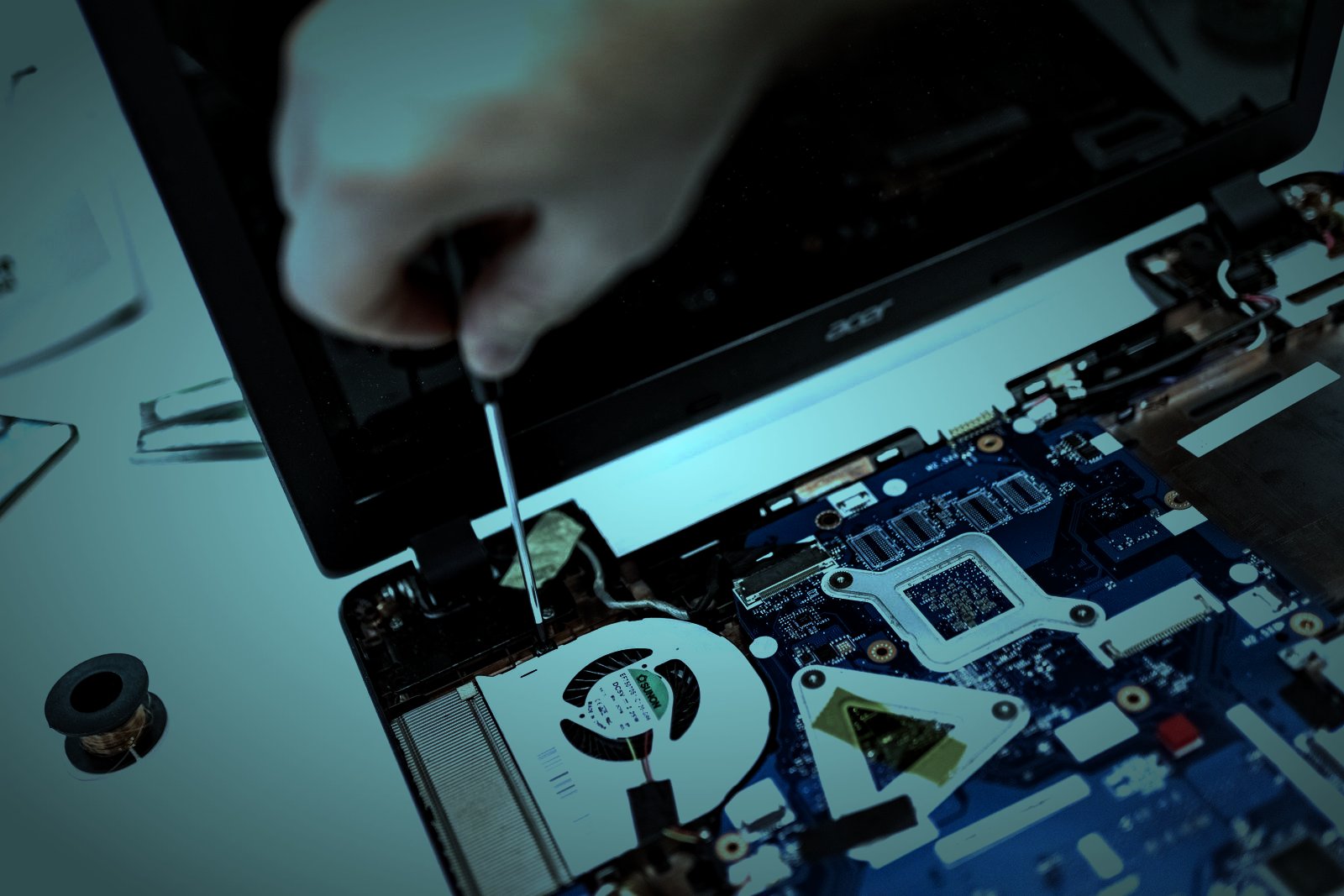 Otwarty laptop na stole serwisowym, dłoń z wkrętakiem nad płytą główną